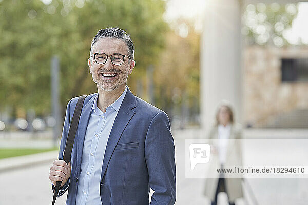 Happy mature businessman wearing eyeglasses on footpath