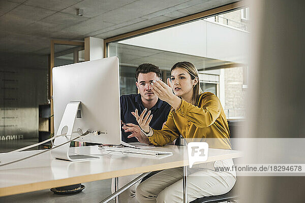 Young businesswoman gesturing and discussing over desktop PC in office