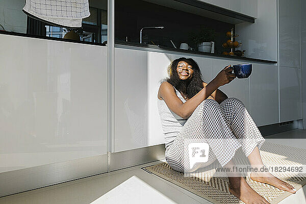 Glückliche Frau sitzt mit Teetasse in der heimischen Küche