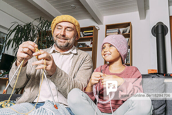 Father and daughter knitting on couch at home together