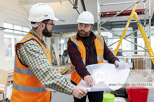 Young engineers wearing protective workwear discussing over blueprint at construction site