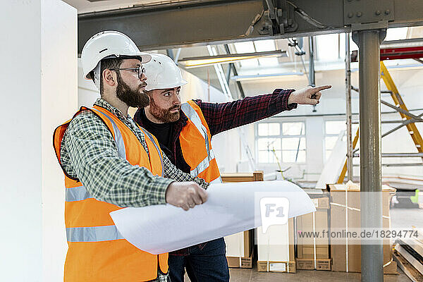 Young engineer gesturing and having discussion with colleague at construction site