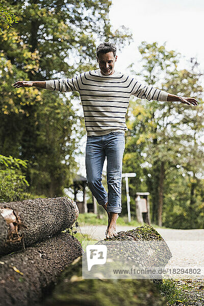 Mature man with arms outstretched walking on log