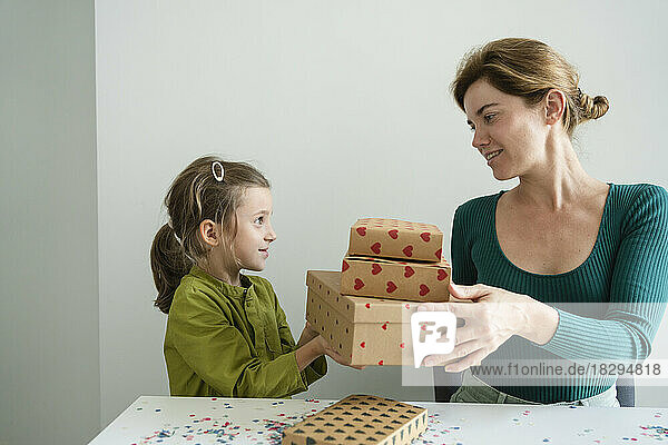 Mother giving stack of gifts to daughter at home