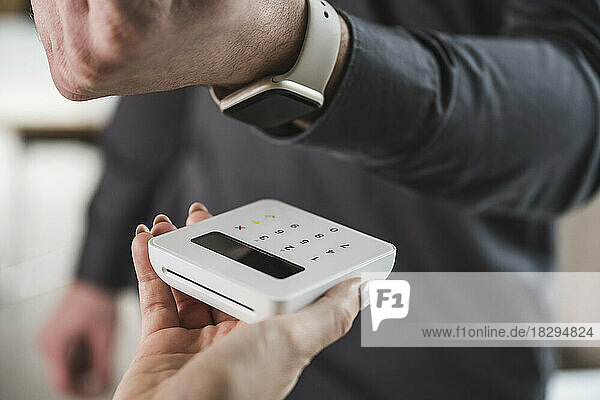 Young businessman paying with smart watch on card reader machine