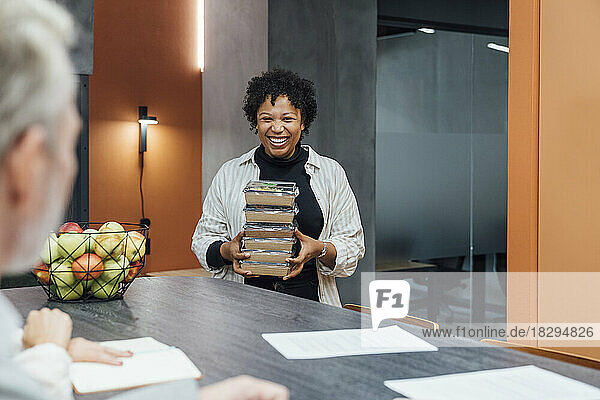 Happy young woman with take away lunch boxes standing by table in office