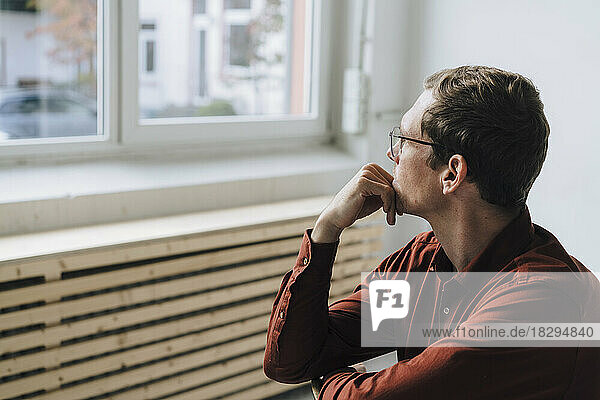 Thoughtful businessman with hand on chin looking through window