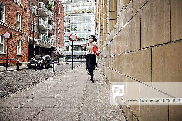 Businesswoman with file folder running on footpath