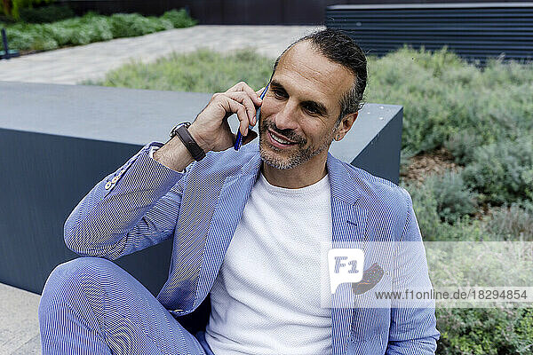 Mature businessman talking over mobile phone sitting on bench