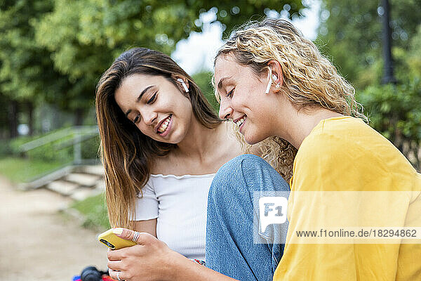 Smiling woman sharing mobile phone with friend in park