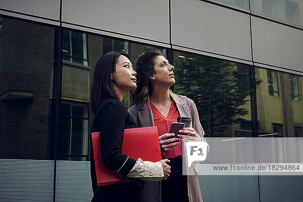 Businesswomen with file folder and smart phone standing in front of building