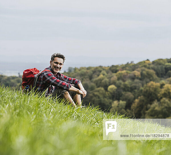 Smiling mature man with backpack sitting in meadow