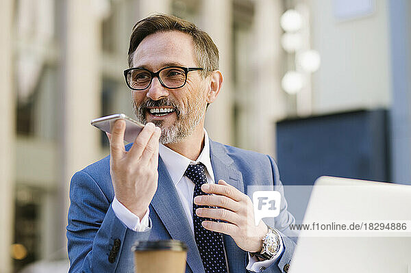 Smiling mature businessman talking on speaker phone at cafe