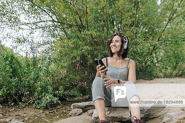 Happy young woman wearing headphones listening to music at park