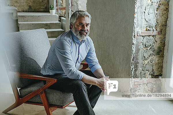 Smiling mature businessman sitting in chair at construction site