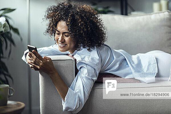 Glückliche Frau  die Textnachrichten über ihr Smartphone sendet und auf dem Sofa liegt