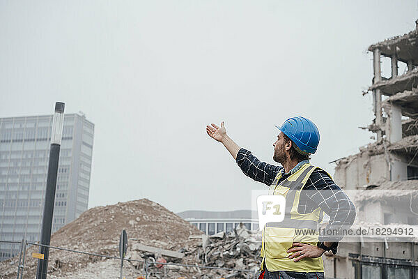 Blue-collar worker wearing hardhat gesturing at construction site