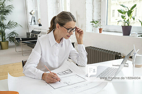 Businesswoman with blueprint looking at laptop at desk in office