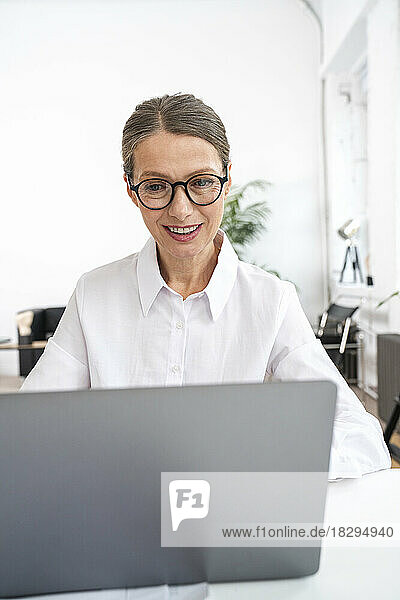 Happy businesswoman wearing eyeglasses using laptop in office