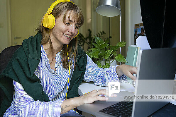 Happy freelancer wearing headphones using smart phone at home