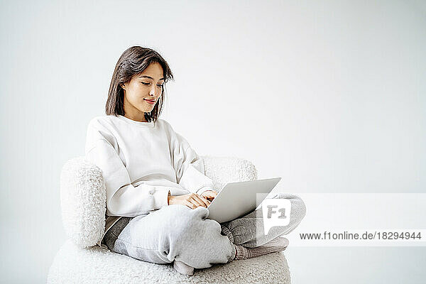 Young woman sitting cross-legged using laptop in front of wall