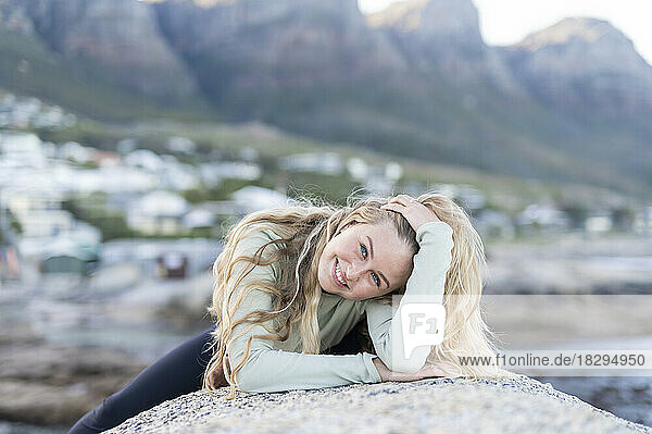 Happy woman with hand in hair lying on rock
