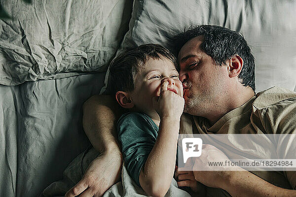 Father kissing cute son in bed