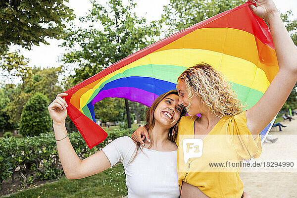 Glückliches lesbisches Paar mit Regenbogenfahne  das sich im Park umarmt