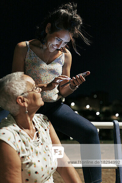 Glückliche junge Frau benutzt Smartphone mit Freund  der im Park sitzt