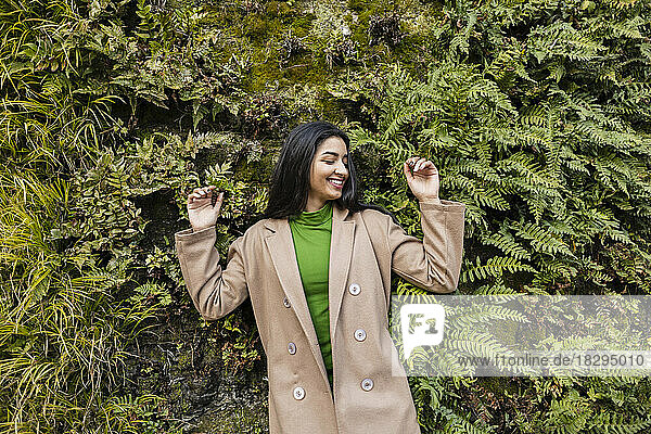 Happy young woman enjoying in front of hedge