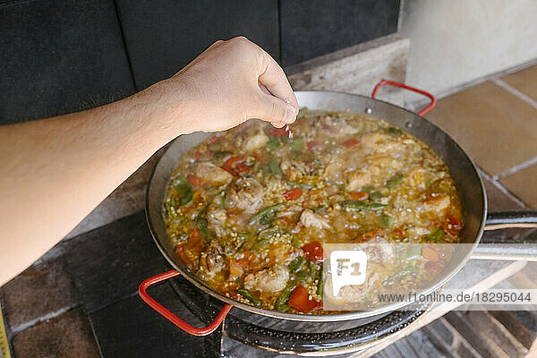 Hand of man adding preparing paella at outdoor kitchen