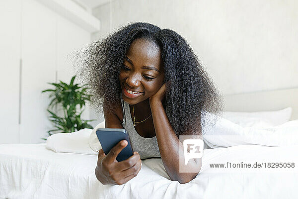 Happy woman lying on bed using mobile phone at home