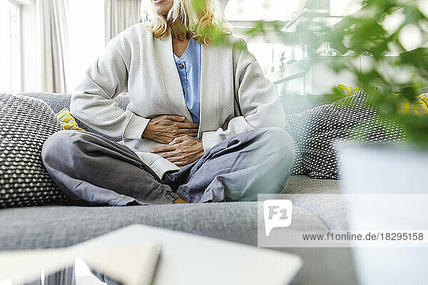 Woman having stomach ache sitting on sofa at home