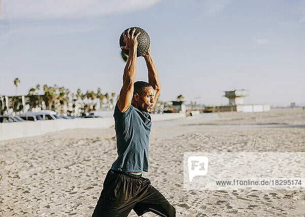 Sportler mit erhobenen Armen trainiert mit Ball am Strand