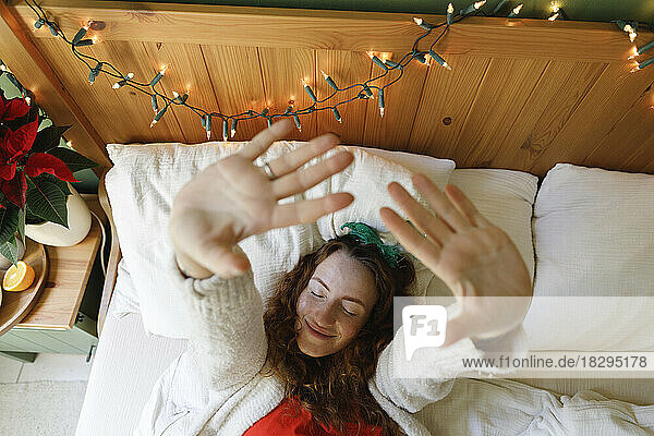 Smiling woman stretching hands lying on bed at home