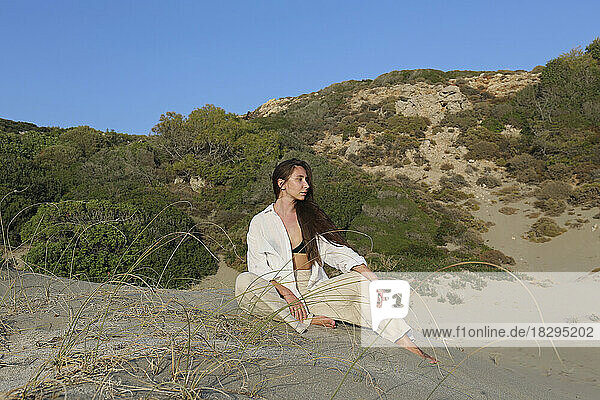 Thoughtful young woman sitting on sand at beach in front of blue sky  Patara  Turkiye