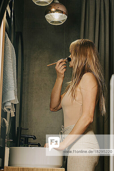 Blond woman applying make-up in bathroom