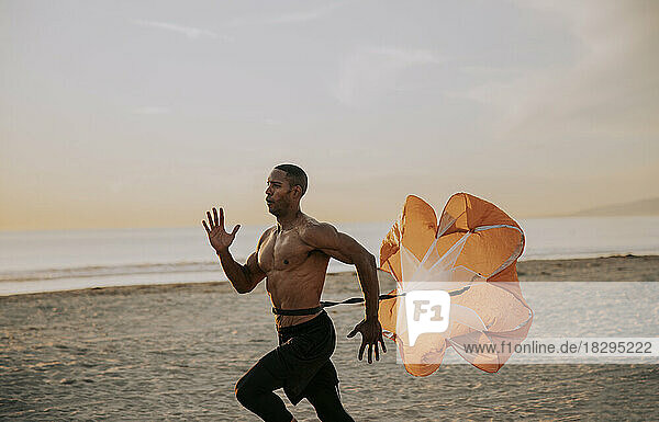 Athlete running with parachute in front of sea at beach