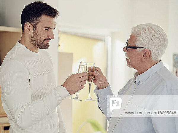 Senior man and adult son tcelebrating at home toasting with champagne