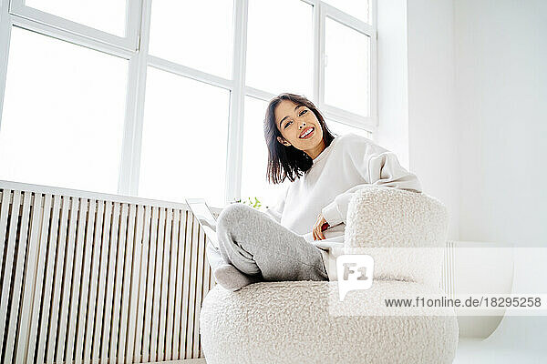 Happy woman with laptop on chair at home