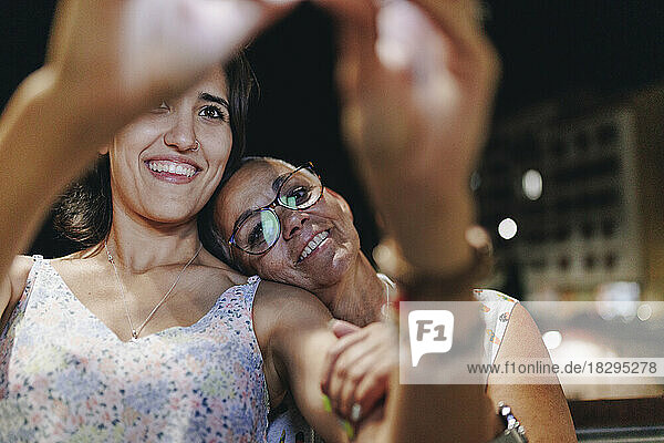 Smiling senior woman leaning head on friend shoulder at night