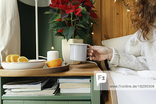 Hand of woman taking mug from side table in bedroom at home