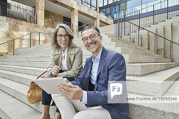 Happy business colleagues with tablet PC sitting on steps