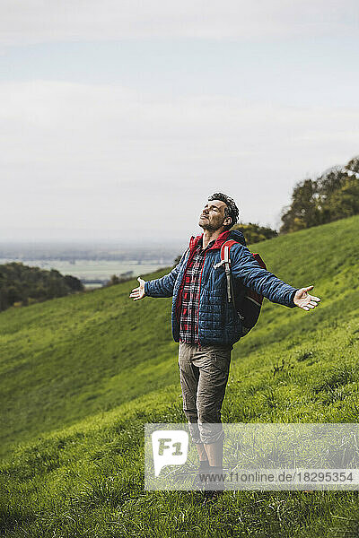 Carefree man with arms outstretched standing on meadow