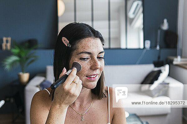 Young woman applying make-up on face at home