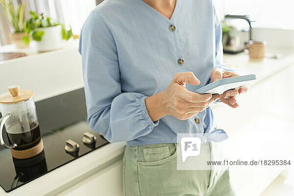 Frau benutzt Smartphone am Tresen in der heimischen Küche