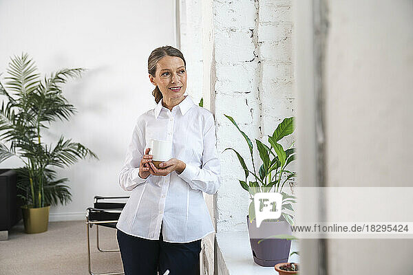 Lächelnde Geschäftsfrau mit Kaffeetasse  die an der Wand steht