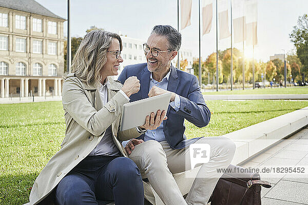 Happy businesswoman giving fist bump to colleague sitting on concrete seat