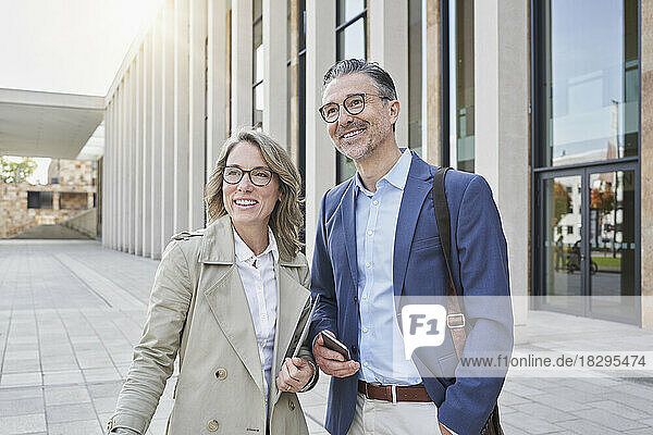 Happy businessman and businesswoman standing outside building