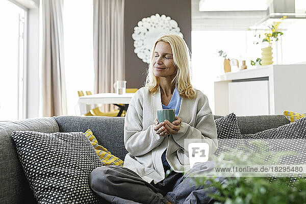 Smiling woman with tea cup sitting on sofa at home